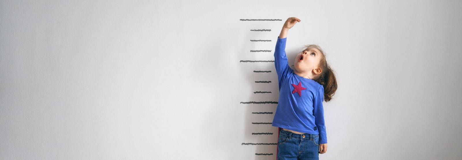 Young girl measuring herself on a growth chart on the wall.